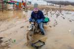 A Syrian refugee rides a motorbike through deep mud at the informal Ta...
