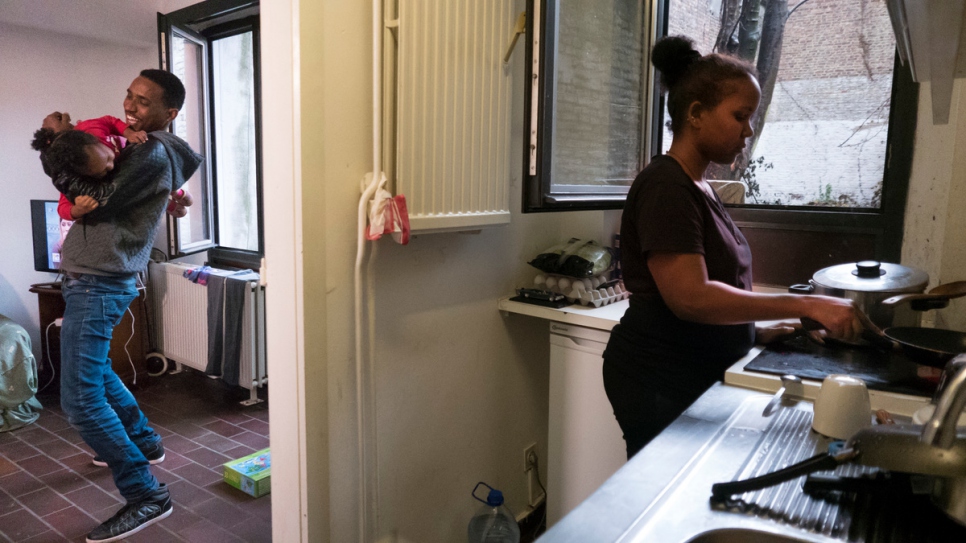 Azoz plays with his two-year old daughter Dina in their home, while Rahel prepares food.