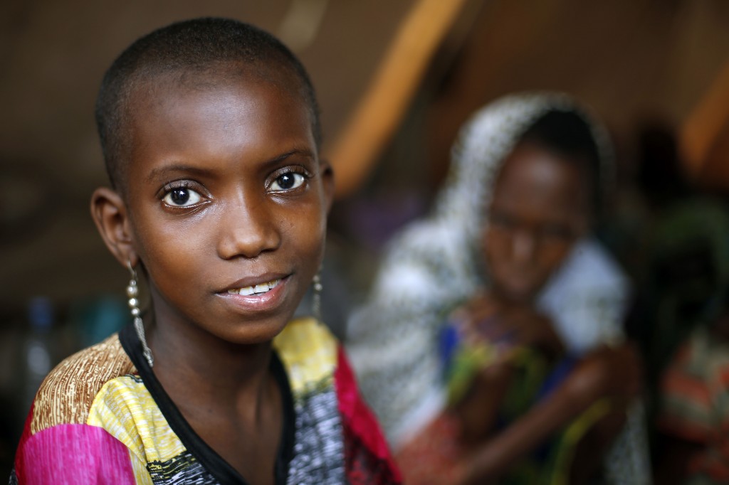 In this April 16, 2014 photo, 10-year-old Hamamatou Harouna smiles as she sits in a tent with other Muslim refugees on the grounds of the Catholic Church in Carnot, Central African Republic. Hammamatou, who had lost the use of her legs to polio, fled Anti-Balaka violence in her village, carried on the back of her 12-year-old brother Souleymane. She spent 10 days alone in the forest. (AP Photo/Jerome Delay)