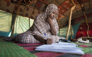 Tinalbarka, uma refugiada de 16 anos do Mali, fazendo seus deveres de casa dentro da tenda de sua família, no campo de refugiados de Mbera.  © ACNUR/ A.Dragaj