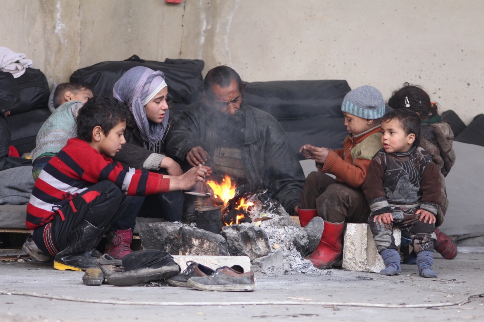 Un homme et ses enfants déplacés tentent de se réchauffer autour d'un feu près du foyer collectif de Jibreen, à Alep.