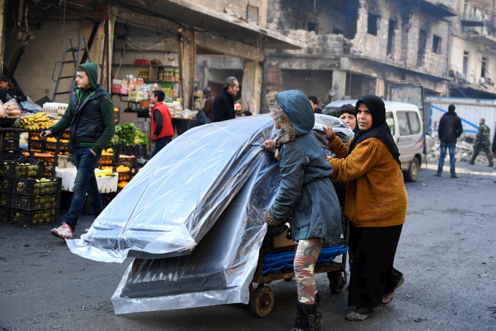 Une femme et ses deux enfants transportent, sur une charrette, des matelas et des articles de secours distribués par le HCR et d'autres partenaires des Nations Unies dans le quartier de Tariq Al-Bab, à Alep-Est.