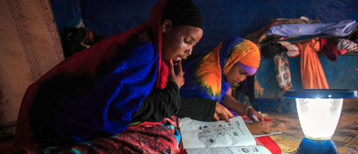 Young refugee girls study next to a solar lamp.