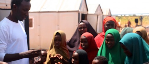 UNHCR staff member Abdiwali Mohamed stands in front of a Better Shelter Unit with refugee youth in Dollo, Ado.