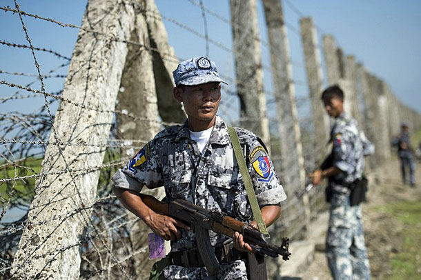 An armed Myanmar border guard walks beside a fence along the river dividing Myanmar and Bangladesh in Maungdaw township, western Myanmar's Rakhine state, Oct. 15, 2016.