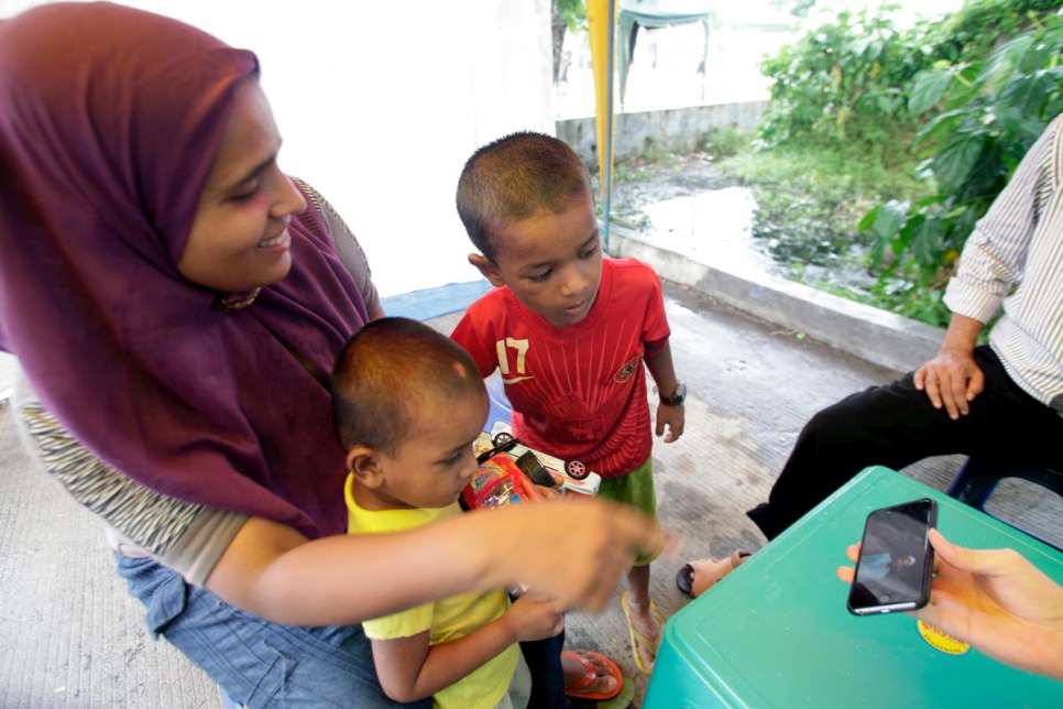 In Aceh, Indonesia, UNHCR staff show Fatima and her sons a photograph of her husband, Hassan, who is in Malaysia.