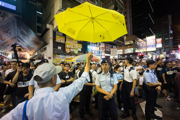 A protester holds a yellow umbrella, the symbol of Hong Kong's pro-democracy movement in front of police in Hong Kong, Aug. 2, 2015.