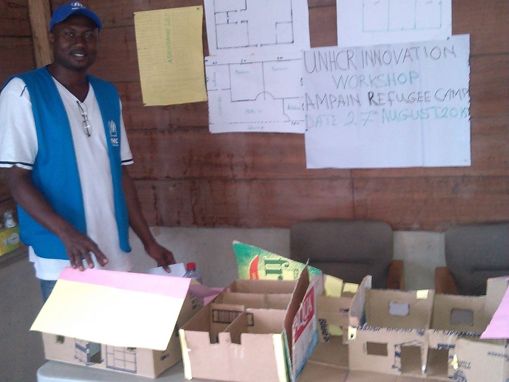 UNHCR Innovation Fellow Yusif stands with prototypes from his brainstorming workshop with refugees on durable housing solutions.