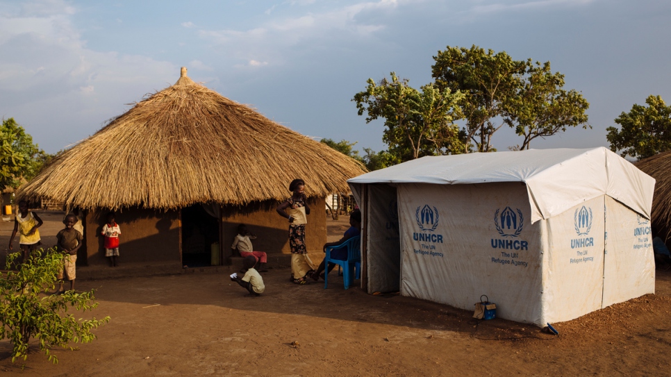 South Sudanese refugee Aisha Christie, 28, outside her shelter in Bidibidi refugee settlement, Yumbe District, Northern Region, Uganda. Christie has two children, Jonathan and thirteen-year old son Godwin. She also cares for her sister's two children – six-year old twins Godfrey and Phillip. In addition, she has recently become a foster parent to a child abandoned in the settlement whom she has named Mercy. She thinks Mercy is about four years old.