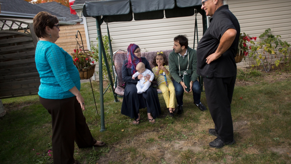 Volunteers Tanna and Joe sit with Husam, Noura, Bayan and six-month-old Adam in the back garden of their house in Peterborough.