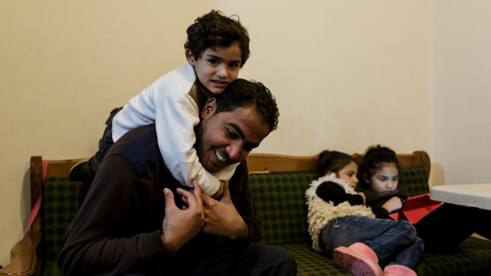 Mohamed's son Baraa plays with his uncle Mofeed, while his sisters watch cartoons on a tablet, inside a house given to the family by UNHCR.