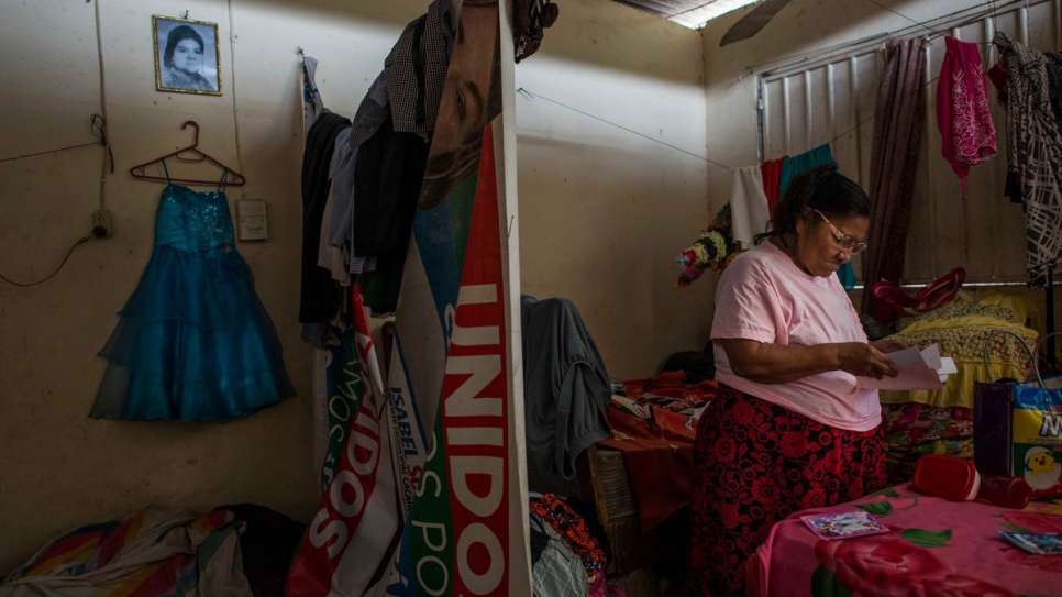 Maria looks at family photos in her room in southern Mexico. The dress hanging on the wall belonged to her great-granddaughter, Maria Luz, who was killed by a gang member in El Salvador.