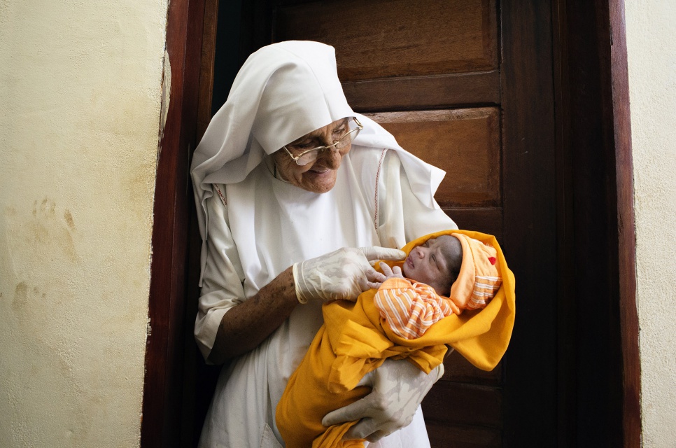 Sister Maria stands outside the delivery room holding a newborn at the hospital her order operates in Zongo, DRC. She has assisted with over 20,000 births.