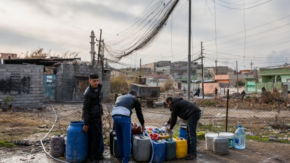 Des hommes remplissent des bidons d'eau en pompant manuellement dans la conduite d'approvisionnement. Les réseaux d'alimentation en eau et en électricité de Mossoul-Est ont été détruits durant les mois de combat et commencent lentement à être restaurés. 