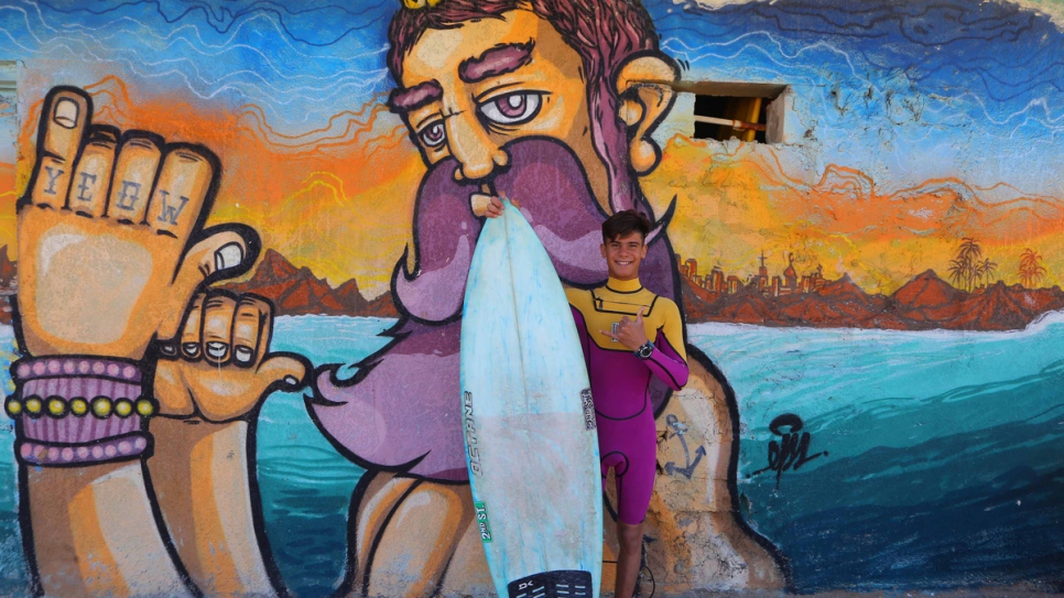 Ali with his surfboard on the beach.