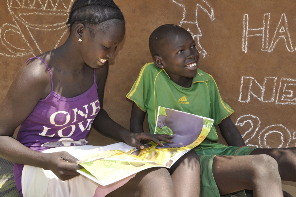 Gur Deng Kuarbang being read to by his older sister – books are lent out by the reading Ambassadors to the children to take home and share with siblings in Kule Camp, Gambella,