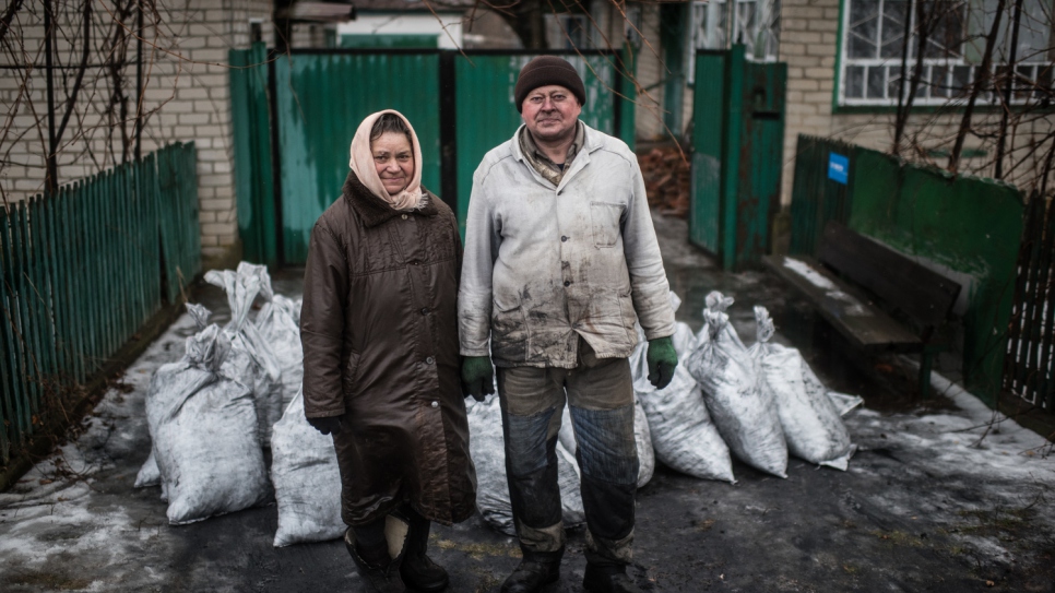 Anna, 68, and Victor, 67, stand in front of several bags of coal that will heat their homes in the village of Luhanske, Donetsk.