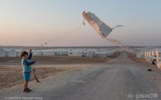 Jordan. Evening view over Azraq Camp. Young Syrian refugee boy flies a homemade kite made from a piece of insulation