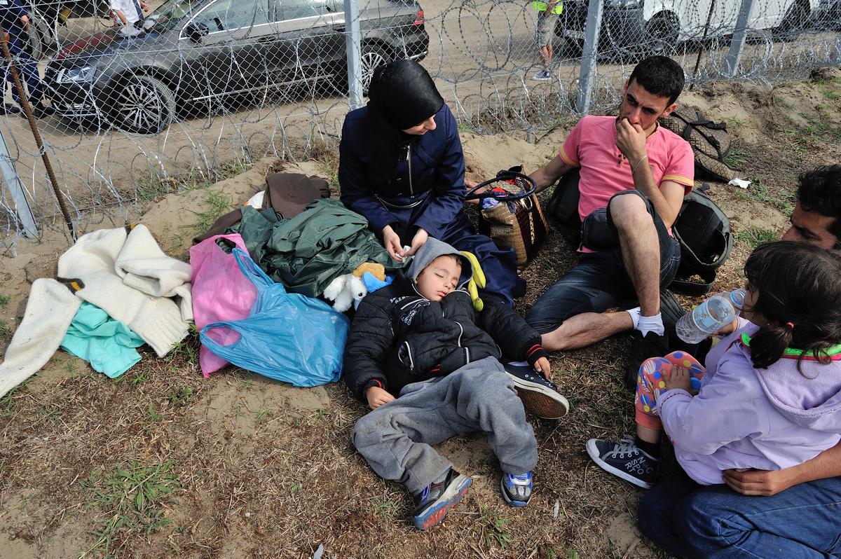 Syrian family sits next to a fence on the Hungarian border with Serbia