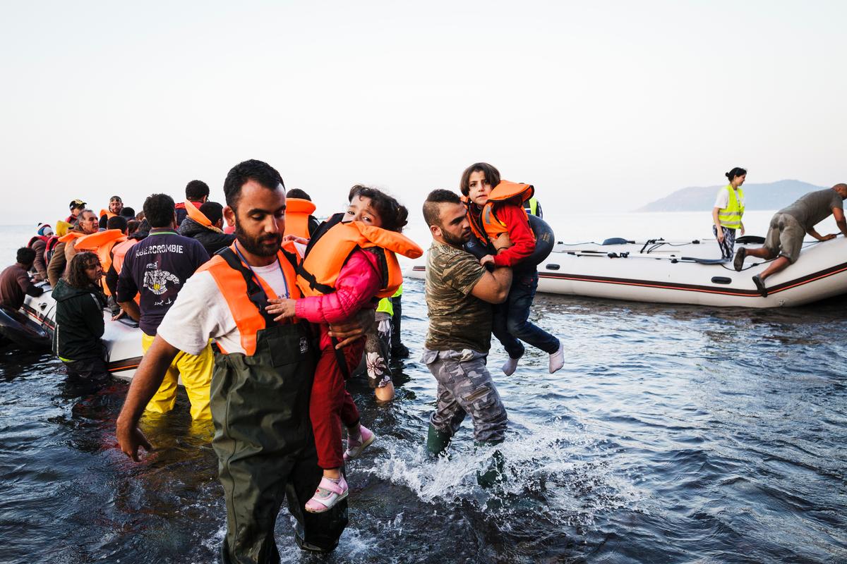 Two young girls are carried from an inflatable boat to the shores of Lesvos, Greece