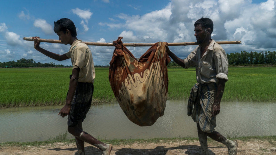 Rohingya refugees Mabia Khatun, 75, (unseen in blanket) is carried by two of her sons after crossing from Myanmar, near Whaikhyang, Bangladesh.