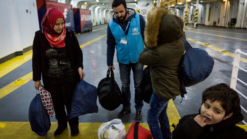 A UNHCR staff member helps Falak and her sons carry their bags onto a ferry bound for Athens.