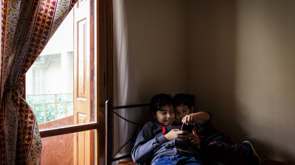 Samir watches cartoons on a cell phone with his younger brother.