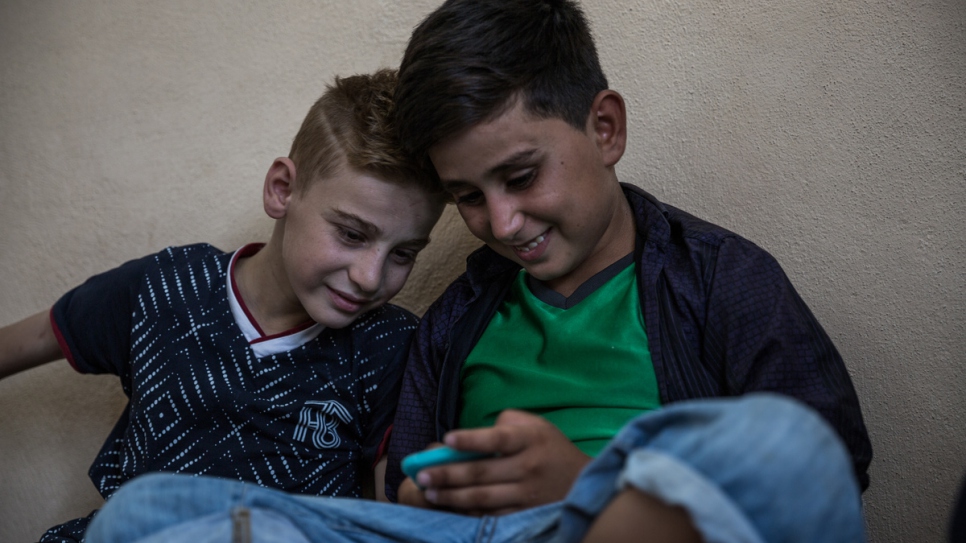 Le jeune yézidi, Emad Tammo (à gauche), regarde les jeux vidéo sur le téléphone cellulaire de son cousin alors qu'il compte les jours à Dohouk, dans la région du Kurdistan d'Iraq, avant de rejoindre sa mère au Canada.