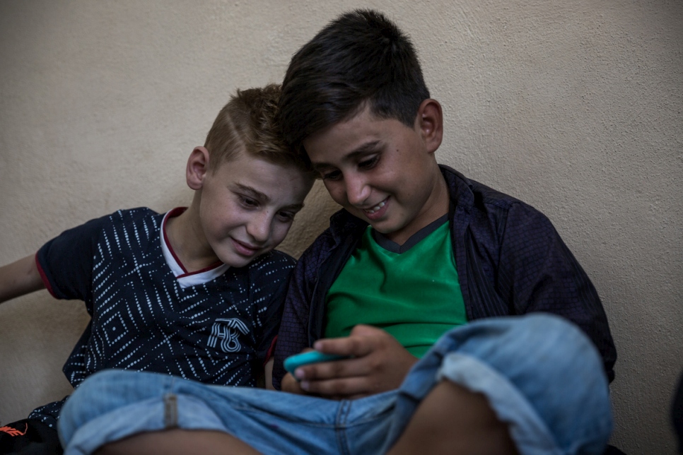 الطفل اليزيدي عماد تامو (يسار) يشاهد ألعاب الفيديو على هاتف ابن عمه فيما يقضي ما تبقى من الوقت في دهوك، كردستان العراق، قبل انضمامه إلى والدته في كندا.
