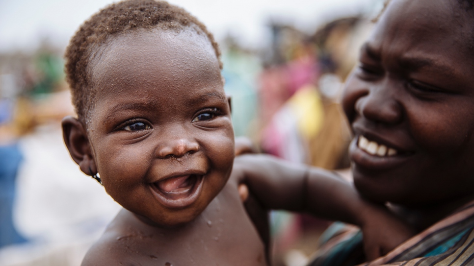 La réfugiée sud-soudanaise Gire Karyot, âgée de sept mois, dont la famille a été déracinée depuis Kajo Keji, au Soudan du Sud, sourit dans les bras de sa Maman au centre de réception d'Imvepi, dans le district d'Arua, dans la région du Nord, en Ouganda. 