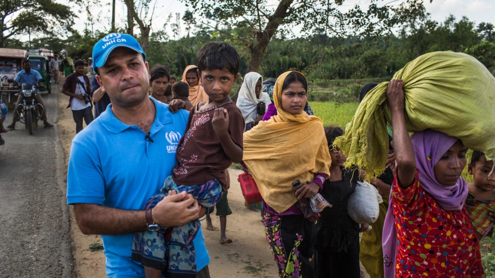 UNHCR spokesman Mohammed Abu Asaker carries Noor Kalima, 4, on the 10-kilometre walk from Myanmar to Kutupalong refugee settlement in Bangladesh. Noor's parents were killed when their village was attacked. Both she and her sister, Umme Salma (wearing black), are being cared for by their aunt, Rabiaa Khatun (wearing orange headscarf).