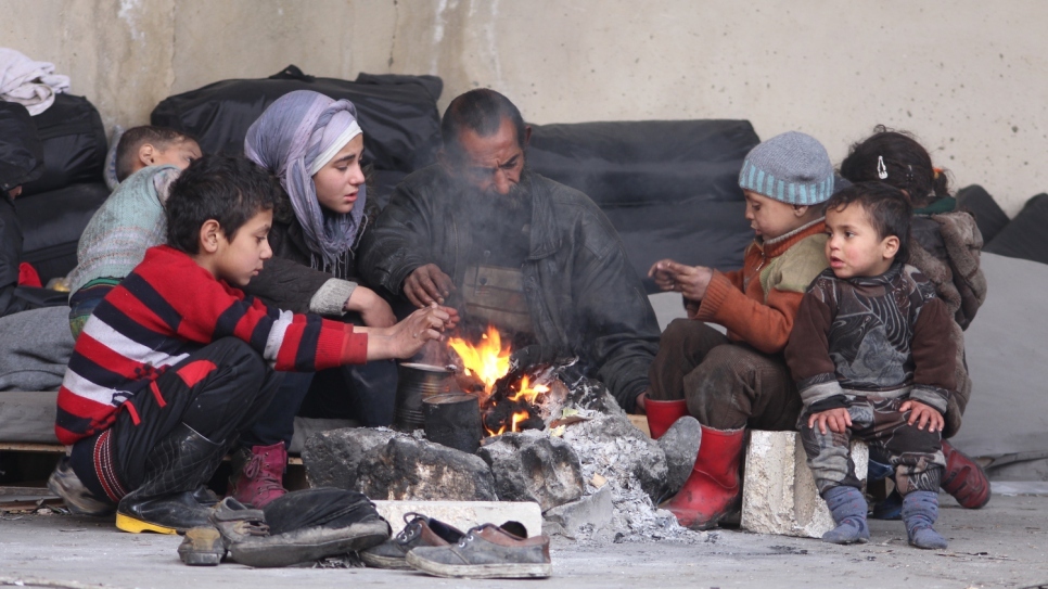 والد نازح وأطفاله يحاولون تدفئة أنفسهم حول النار في مأوى جبرين الجماعي في حلب.