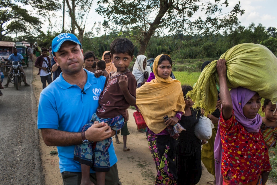 المتحدث باسم المفوضية محمد أبو عساكر يحمل الطفلة نور أثناء مسيرها لـ10 كيلومترات من حدود ميانمار إلى مركز النقل التابع للمفوضية في كوتوبالونغ، بنغلاديش. قتل والدا نور إثر هجومٍ تعرضت له قريتهم، والآن هي وأختها أم سلمة تعيشان مع خالتهما ربيعة. (في الوشاح البرتقالي).
