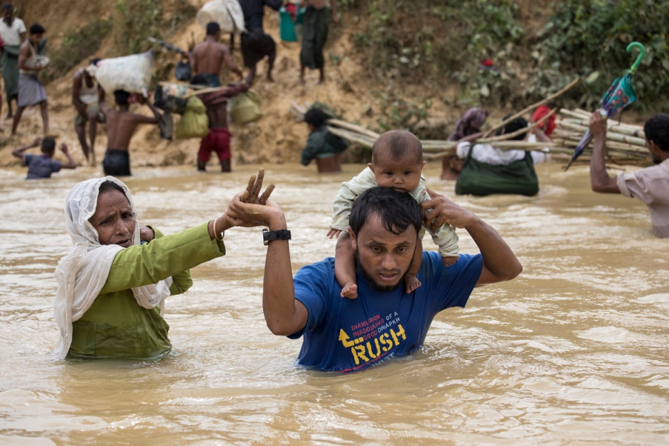 عائلة من اللاجئين الروهينغا من ميانمار تعبر نهراً فائضاً نتيجة الأمطار في مخيم كوتوبالونغ في بنغلاديش. 