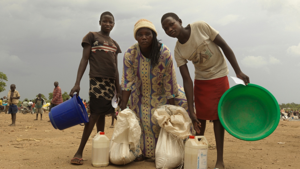 Tabu collecte l'aide alimentaire de sa famille avec sa mère adoptive (centre) et sa soeur jumelle (à droite).