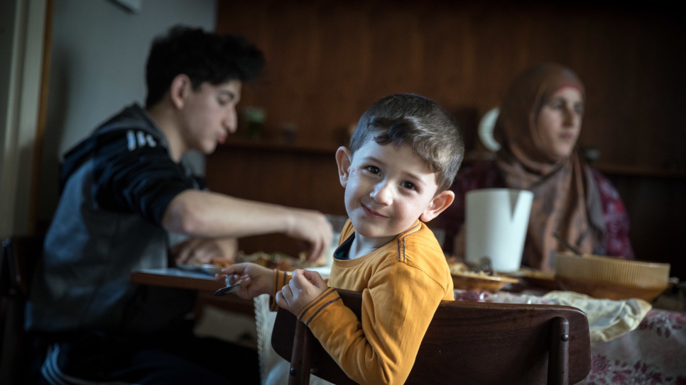 A younger member of the extended family, now reunited in Austria, enjoys a meal with his mother and cousin.