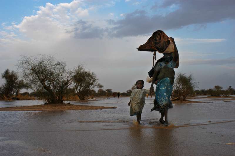A refugee family carrying their belongings out of the water after their makeshift shelter was flooded when the first heavy rains near Bahai swelled the seasonal riverbed. The flooded-out refugees were immediately transferred to a new camp that had just opened to receive them. (July 14, 2004)