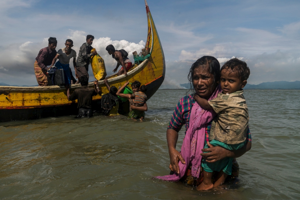 Une mère portant son enfant dans ses bras marche dans l'eau vers la plage de Dakhinpara, au Bangladesh. 