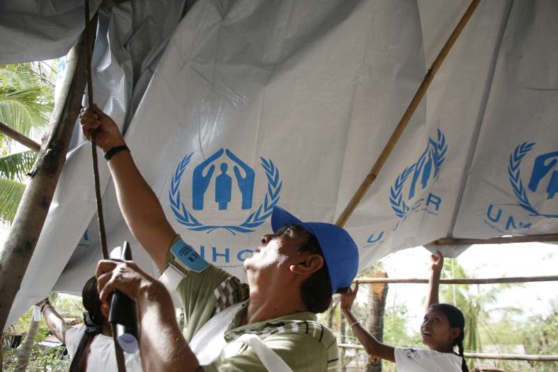 UNHCR staff help a family build a temporary roof with plastic sheeting after their home was destroyed by Cyclone Nargis.