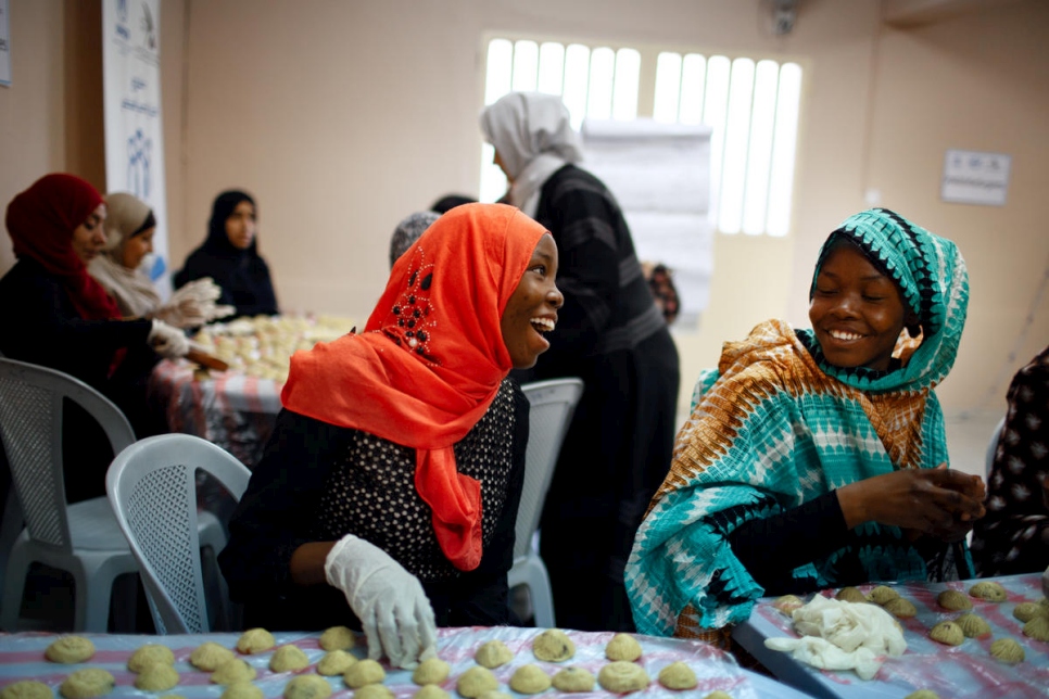 الأختان السودانيتان اللاجئتان زينب عبدالله (يسار بالأحمر) ونهى (يمين) تصنعان حلويات عربية للعيد في مركز الأميرة بسمة للتنمية الاجتماعية في عمَّان، الأردن.