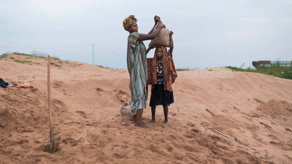A Congolese mother and child who have been displaced by conflict work an early-morning shift packing and transporting sand from Lake Tanganyika to local construction sites.