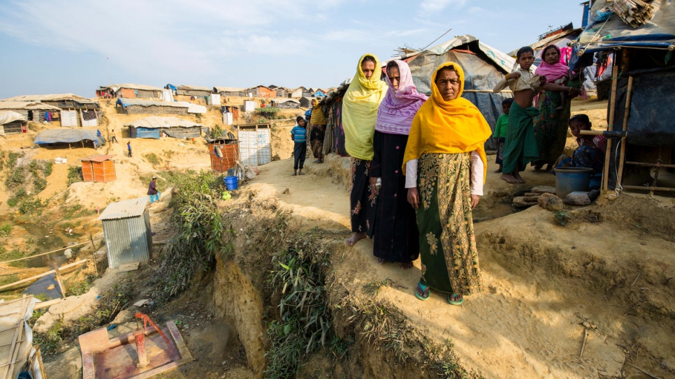 Siraj Begum, 38, yellow scarf, Mariam Khatun, 60, violet scarf, and Nur Nahar, 45, orange scarf, stand outside their shelter in Kutupalong refugee settlement, Bangladesh. Their home is on a steep hillside deemed at risk of collapse in the monsoon rains.