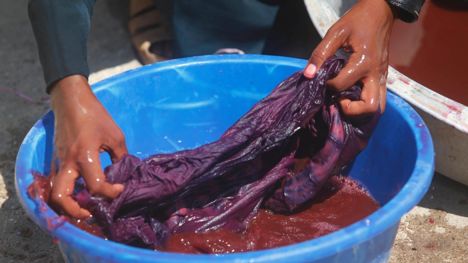  The cloth is submerged in a bucket of dye before being hung out to dry.