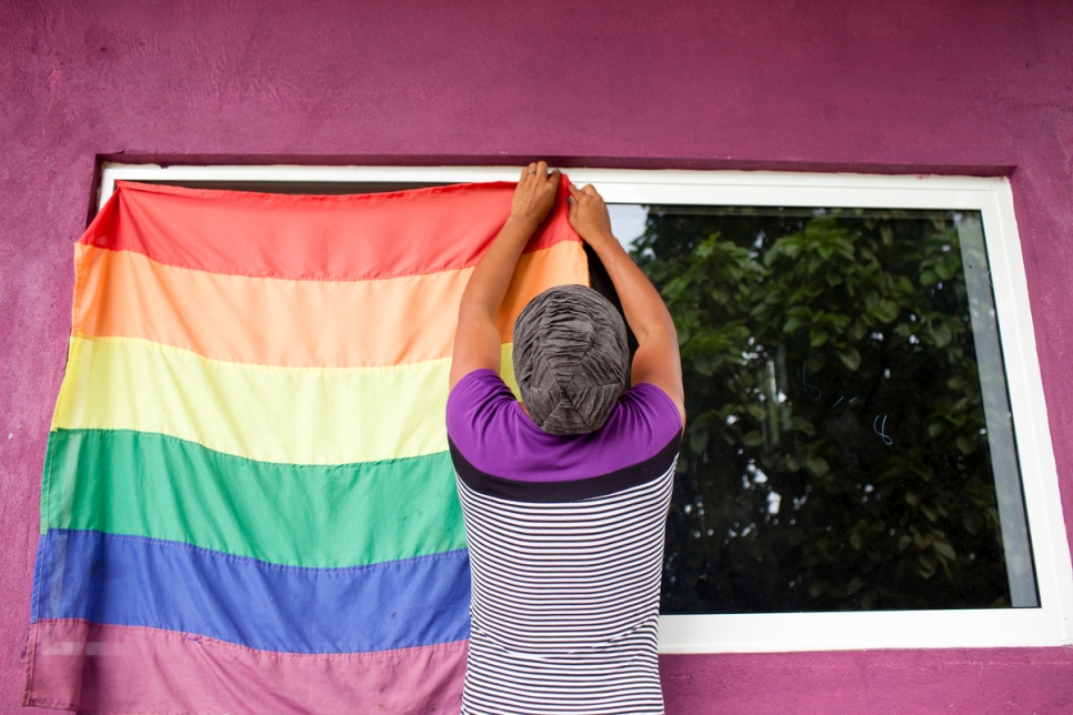 A person hangs a rainbow flag to a window.