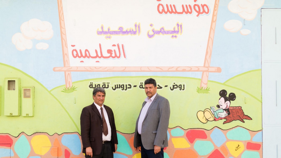 Abdullah (right) stands outside the school building with a member of staff.