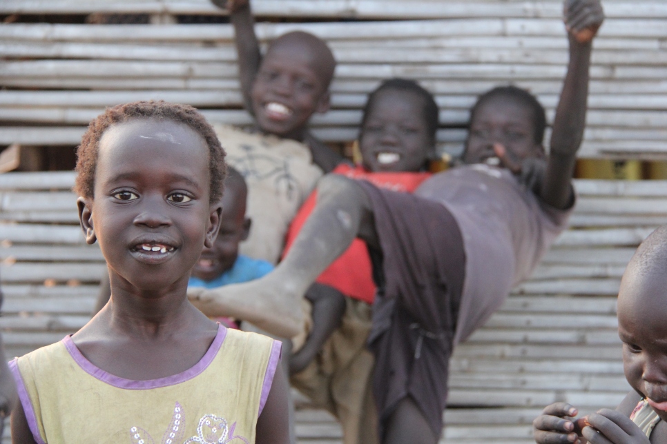 Ayuel, 8, poses for a photograph in Nyumanzi settlement, as her siblings play around in the background. She goes to Nyumanzi 1 primary school and is in Primary 1 (grade 1).