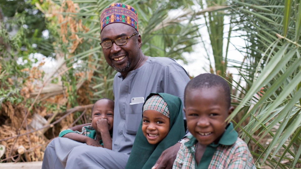Mustapha y tres de sus niños sentados en el jardín de su casa junto a la primera escuela para huérfanos y otros niños que fundó en Maiduguri, estado de Borno, Nigeria, lugar azotado por el conflicto.