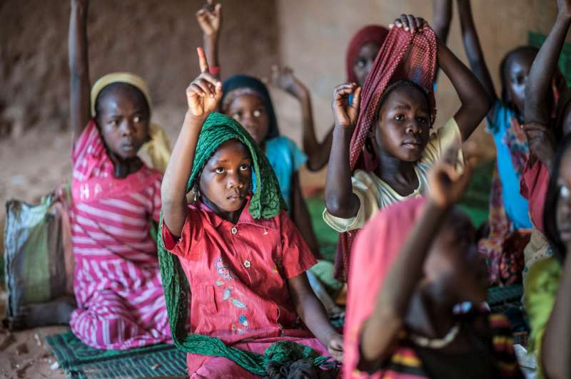 Child refugee Zoera, in faded red dress with green headscarf, attends class at Djabal camp in Chad