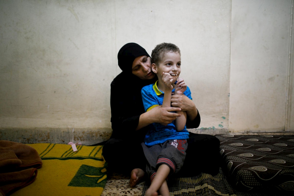 اللاجئة السورية غانية حموي، من حمص، تلعب مع ابنها عبد الهادي في منزلهما في مخيم الحسين الحضري للاجئين  في الأردن، وقد استلمت حلويات صنعتها لاجئات ومستضيفاتهن الأردنيات في عمان، الأردن.