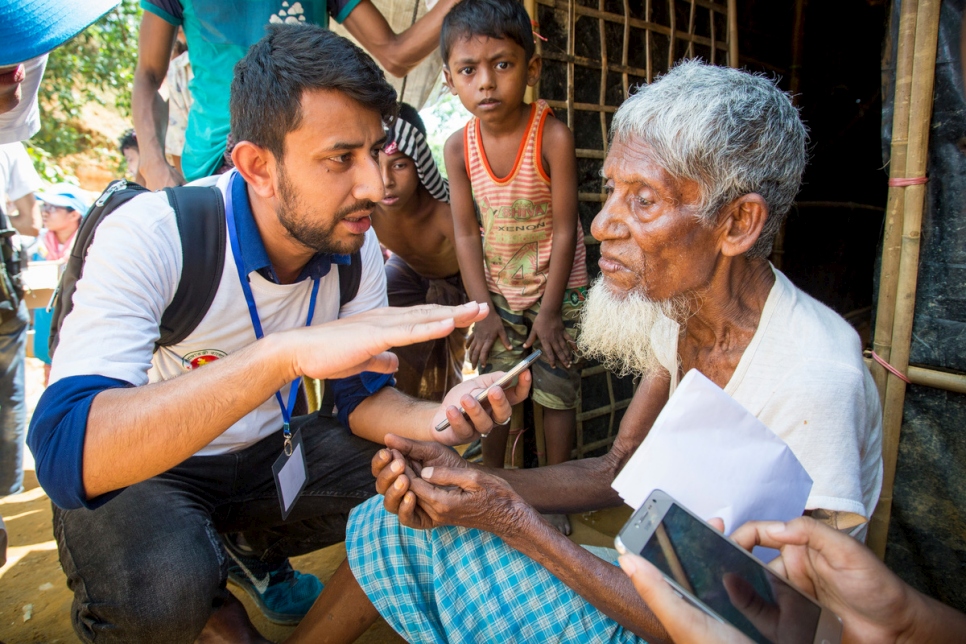 A UNHCR contractor collects information from Mohammad Busho, 80, using a data-gathering smartphone app that helps to streamline assistance at the Kutupalong extension site, Bangladesh